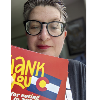 Seana holding up a Colorado postcard that reads Thank you for voting in 2020!