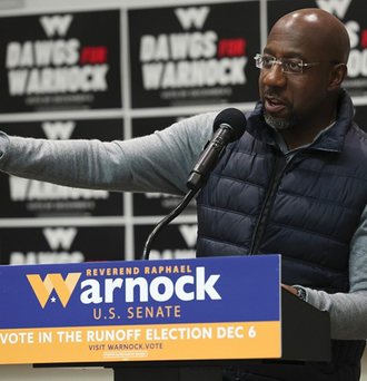 Raphael Warnock speaks into a microphone behind a podium that reads Reverend Raphael Warnock for US Senate