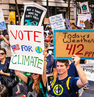 Protesters at a rally holding signs that read "Vote for Climate" and "Today's Weather: 412 PPM"